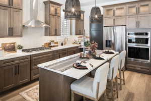 Kitchen featuring appliances with stainless steel finishes, backsplash, wall chimney exhaust hood, decorative light fixtures, and light hardwood / wood-style floors