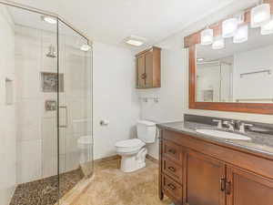 Bathroom with a shower with door, vanity, a textured ceiling, and toilet