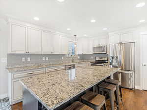 Kitchen with white cabinets, hanging light fixtures, and appliances with stainless steel finishes