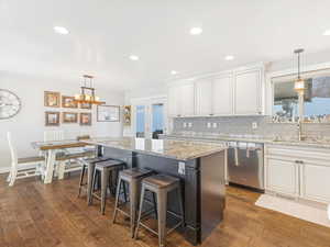 Kitchen featuring stainless steel dishwasher, decorative backsplash, a center island, and white cabinetry