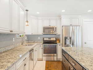 Kitchen with sink, white cabinetry, stainless steel appliances, and hanging light fixtures