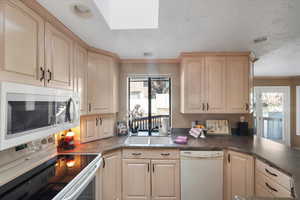 Kitchen with blonde cabinetry, smooth top range & solid surface counters