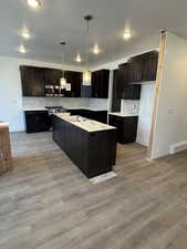 Kitchen with decorative light fixtures, stainless steel appliances, a kitchen island, and light hardwood / wood-style flooring