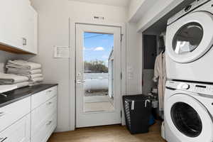 Washroom with cabinets, stacked washing maching and dryer, and light hardwood / wood-style floors