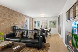 Living room with a fireplace, light hardwood / wood-style flooring, and brick wall