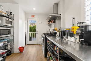 Kitchen with stainless steel counters, light hardwood / wood-style floors, stainless steel appliances, and range hood