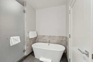 Bathroom featuring tile patterned flooring, a bath, and tile walls