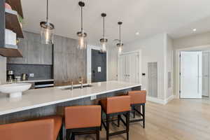 Kitchen featuring decorative backsplash, light wood-type flooring, a breakfast bar, sink, and decorative light fixtures