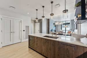 Kitchen featuring dark brown cabinets, beverage cooler, sink, decorative light fixtures, and light hardwood / wood-style flooring