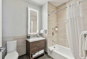 Full bathroom featuring shower / bathtub combination with curtain, tile patterned floors, toilet, vanity, and tile walls