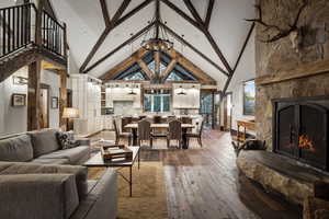 Living room with beamed ceiling, high vaulted ceiling, hardwood / wood-style floors, a fireplace, and ceiling fan with notable chandelier