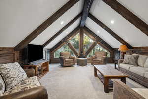 Carpeted living room with vaulted ceiling with beams and wooden walls