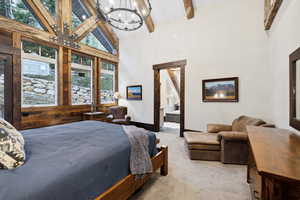 Carpeted bedroom with beam ceiling, connected bathroom, an inviting chandelier, and high vaulted ceiling