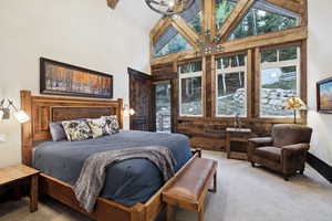 Carpeted bedroom with an inviting chandelier, high vaulted ceiling, and wood walls