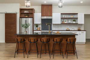 Kitchen with open shelves, white cabinets, tasteful backsplash, high quality fridge, and a breakfast bar area