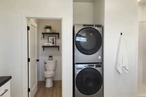 Washroom featuring light wood-style flooring, stacked washer and clothes dryer, wainscoting, and tile walls