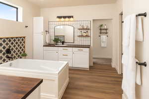Bathroom with vanity, a garden tub, dark wood finished floors, and decorative backsplash