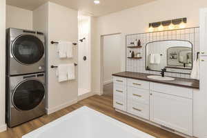 Bathroom with vanity, a walk in shower, stacked washer / drying machine, dark wood finished floors, and recessed lighting