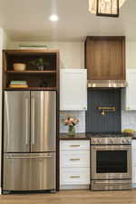 Kitchen with white cabinetry, stainless steel appliances, tasteful backsplash, exhaust hood, and open shelves
