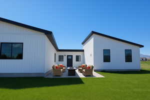 Back of property with an outdoor living space with a fire pit, a patio, and a lawn