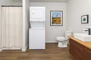 Bathroom featuring vanity, dark wood finished floors, stacked washer / drying machine, and shower / bathtub combination with curtain