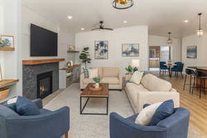 Living room with a tiled fireplace, light wood finished floors, recessed lighting, lofted ceiling, and ceiling fan