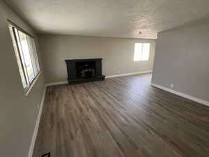 Unfurnished living room with hardwood / wood-style floors, a textured ceiling, and a brick fireplace