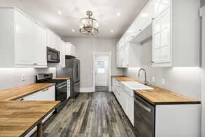 Kitchen with stainless steel appliances, sink, an inviting chandelier, butcher block countertops, and white cabinetry