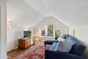 Living room featuring a textured ceiling, hardwood / wood-style flooring, and vaulted ceiling