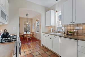 Kitchen featuring white appliances, sink, hanging light fixtures, tasteful backsplash, and white cabinetry