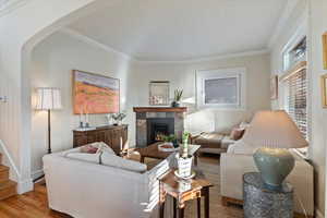 Living room featuring light wood-type flooring, ornamental molding, and a tiled fireplace