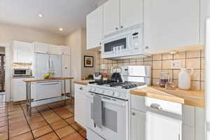 Kitchen featuring tasteful backsplash, light tile patterned floors, white cabinets, and white appliances