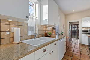 Kitchen with white cabinets, sink, backsplash, and white dishwasher