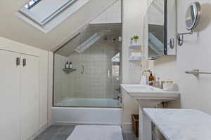 Bathroom featuring shower / bath combination with glass door, tile patterned flooring, and lofted ceiling with skylight