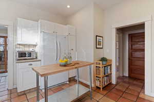 Kitchen with wood counters, tasteful backsplash, light tile patterned floors, white cabinets, and white fridge