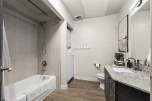 Full bathroom with tiled shower / bath, stacked washer / dryer, toilet, vanity, and hardwood / wood-style flooring