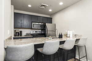 Kitchen with a breakfast bar, light stone counters, kitchen peninsula, and stainless steel appliances