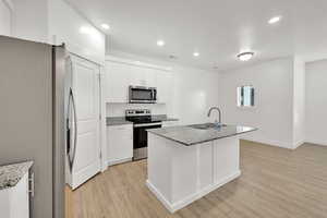 Kitchen with a kitchen island with sink, sink, light stone counters, white cabinetry, and stainless steel appliances