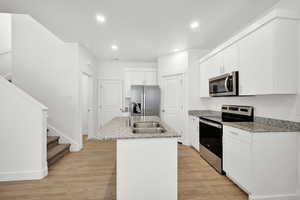 Kitchen with a center island with sink, white cabinets, sink, light wood-type flooring, and stainless steel appliances