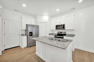 Kitchen with white cabinetry, sink, light stone countertops, light hardwood / wood-style floors, and appliances with stainless steel finishes