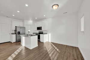 Kitchen featuring a kitchen island with sink, hardwood / wood-style floors, white cabinets, and appliances with stainless steel finishes