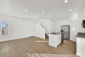 Kitchen featuring appliances with stainless steel finishes, sink, white cabinets, light hardwood / wood-style floors, and an island with sink