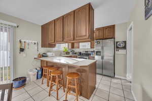 Kitchen with sink, kitchen peninsula, a breakfast bar, light tile patterned flooring, and appliances with stainless steel finishes