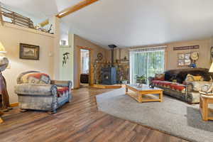 Living room featuring hardwood / wood-style floors, vaulted ceiling with beams, and a wood stove