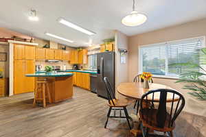 Kitchen featuring stainless steel appliances, decorative light fixtures, light hardwood / wood-style floors, a kitchen island, and lofted ceiling