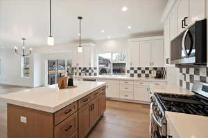 Kitchen with stainless steel gas range oven, a kitchen island, pendant lighting, decorative backsplash, and white cabinets.