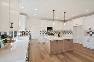 Kitchen featuring appliances with stainless steel finishes, decorative light fixtures, a kitchen island, and white cabinets.