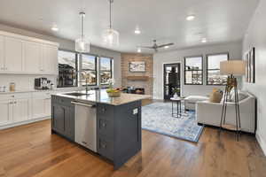 VIRTUALLY STAGED - Kitchen featuring pendant lighting, dishwasher, a kitchen island with sink, sink, and white cabinetry