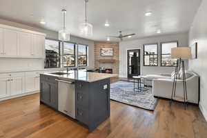 Kitchen featuring white cabinetry, sink, hanging light fixtures, stainless steel dishwasher, and a center island with sink