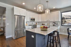 VIRTUALLY STAGED - Kitchen featuring a kitchen island with sink, white cabinetry, pendant lighting, and premium appliances